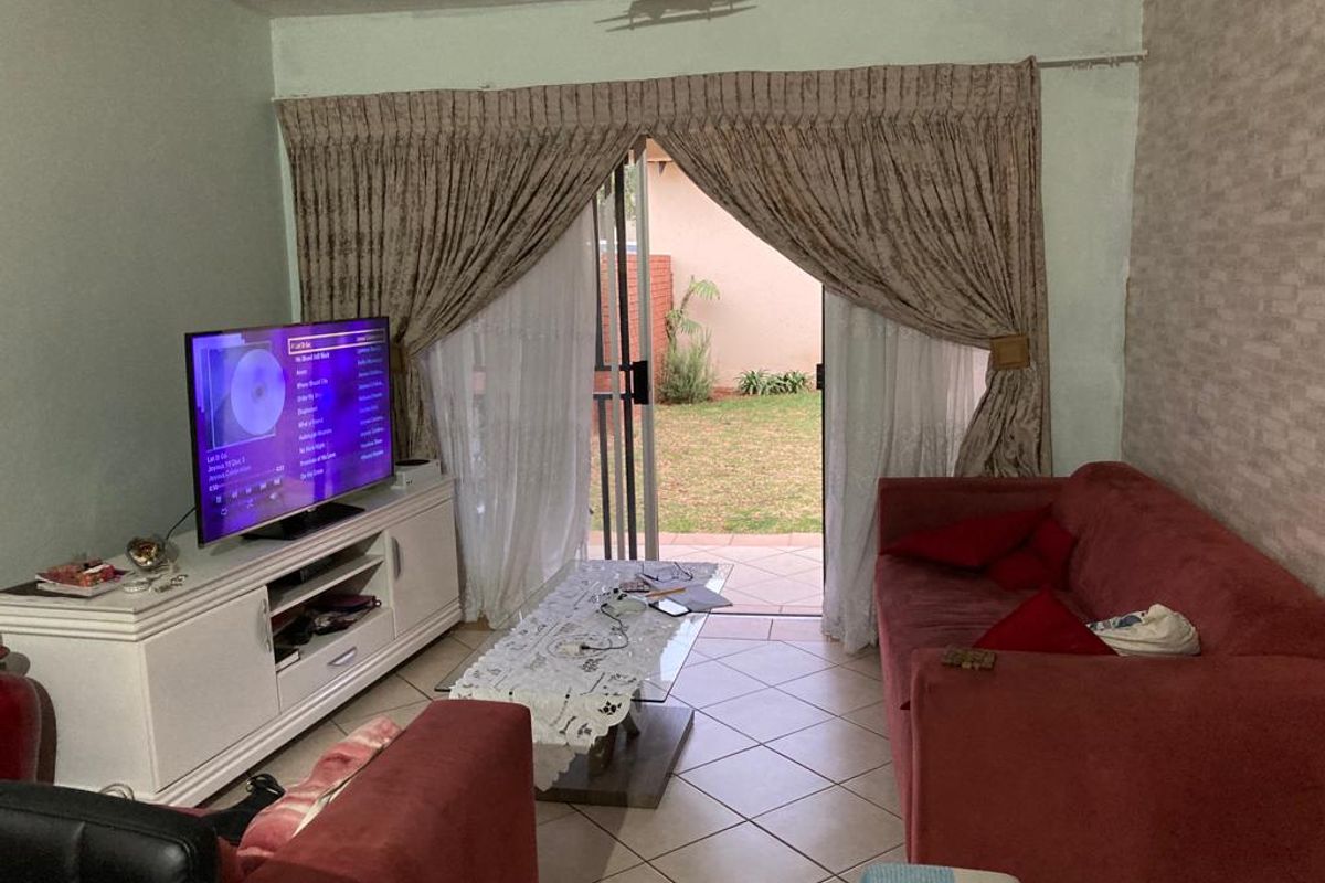 A living room featuring ceramic floor tiles, textured wallpaper, and a sliding glass door providing direct access to the rear patio and garden area.