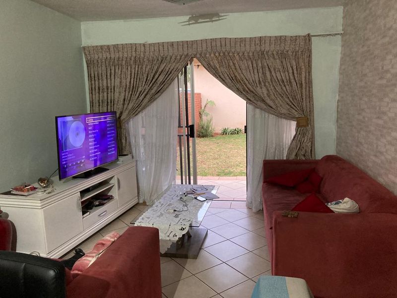 A living room featuring ceramic floor tiles, textured wallpaper, and a sliding glass door providing direct access to the rear patio and garden area.
