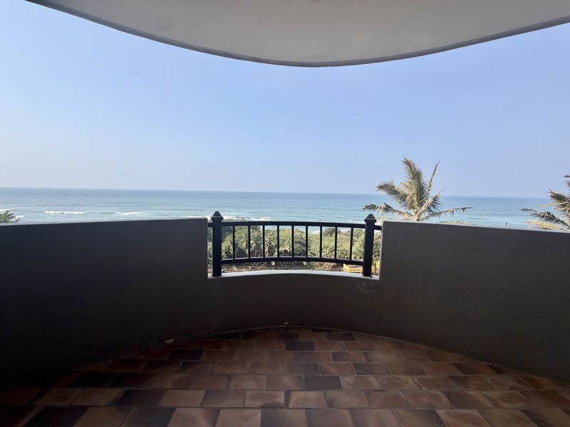 A spacious curved balcony featuring tiled flooring and a metal balustrade, offering expansive, unobstructed views of the ocean.