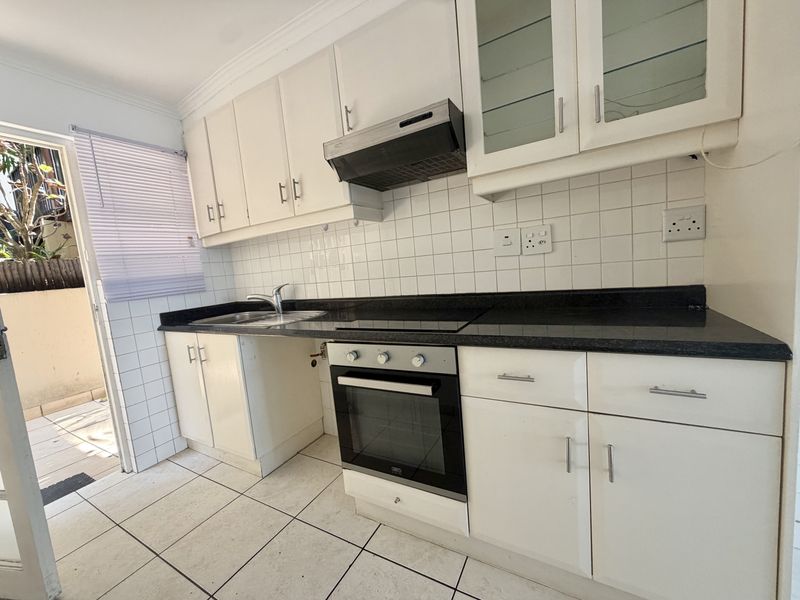 A functional kitchen featuring white cabinetry, granite countertops, a built-in oven with hob, and direct access to an outdoor patio area.