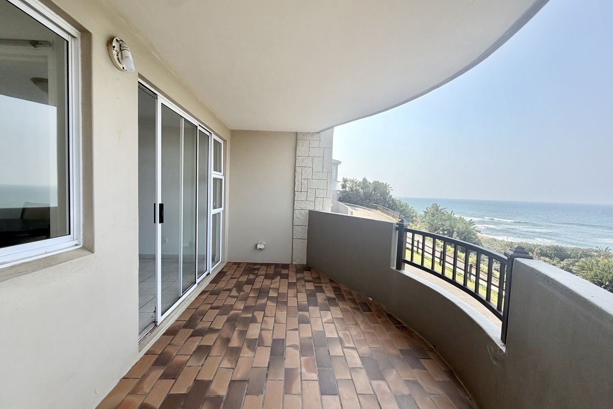 Spacious covered balcony featuring tiled flooring, a metal balustrade, and stunning ocean views, providing an ideal outdoor space for relaxation.