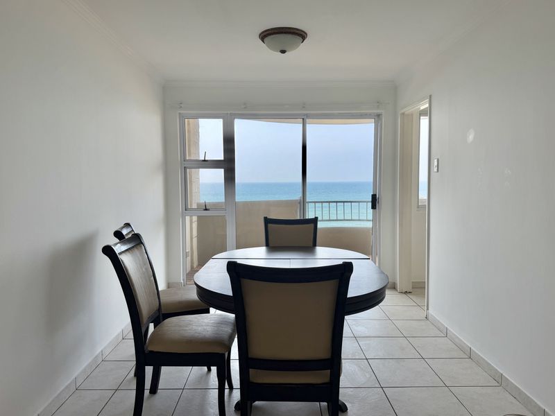 A dining area featuring tiled flooring and a sliding glass door that opens to a balcony with ocean views.
