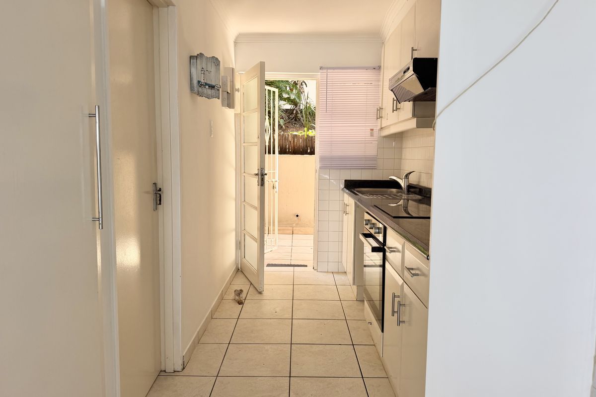 A compact, functional kitchen featuring built-in cabinetry, integrated appliances, and tiled finishes, with direct access to an outdoor patio area.