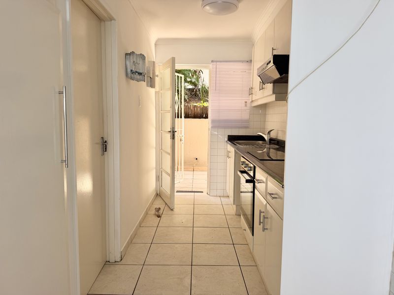 A compact, functional kitchen featuring built-in cabinetry, integrated appliances, and tiled finishes, with direct access to an outdoor patio area.
