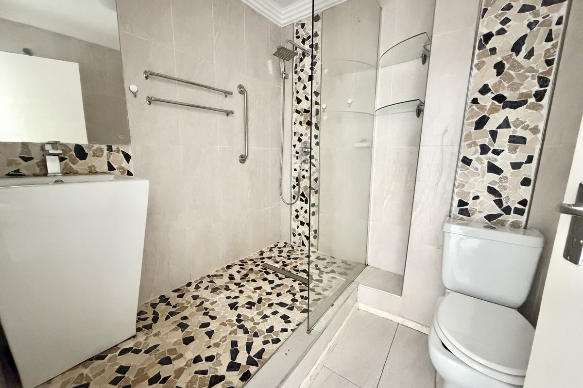 A functional bathroom featuring a walk-in shower with a rain shower head, mosaic tile detailing, a pedestal basin, and a standard toilet.