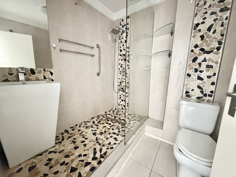 A functional bathroom featuring a walk-in shower with a rain shower head, mosaic tile detailing, a pedestal basin, and a standard toilet.