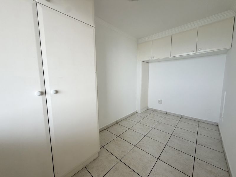 A clean, empty bedroom featuring white built-in cupboards, overhead storage units, and neutral tiled flooring with crown molding details.