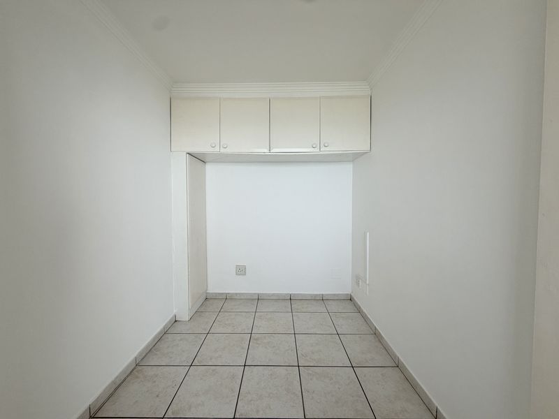 An empty bedroom featuring tiled flooring, coved ceiling cornices, and built-in overhead storage cupboards.