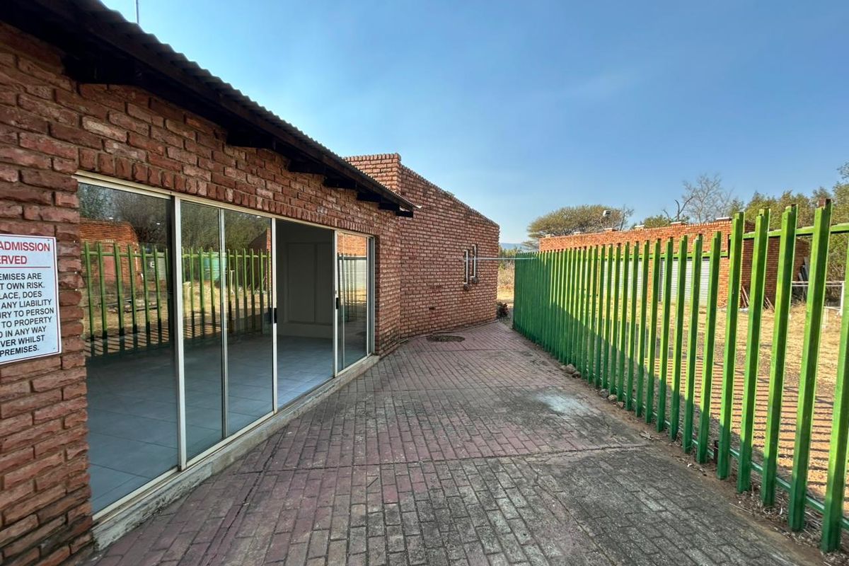 Exterior view of a brick building featuring sliding glass doors, a paved walkway, and secure metal perimeter fencing.