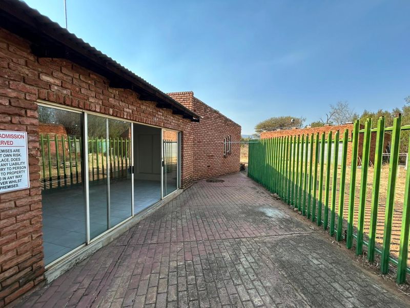 Exterior view of a brick building featuring sliding glass doors, a paved walkway, and secure metal perimeter fencing.