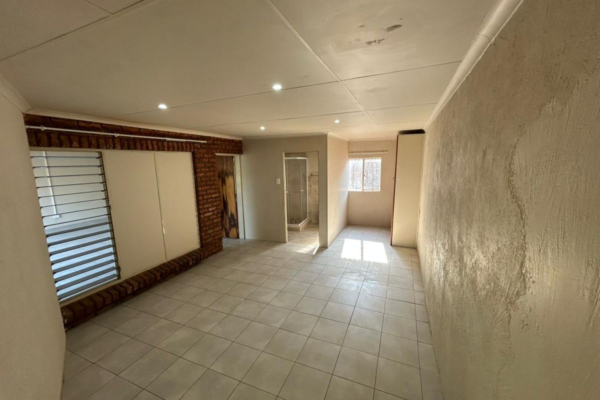 An empty bedroom featuring tiled floors, an exposed brick accent wall, recessed lighting, and an attached en-suite bathroom with a shower.