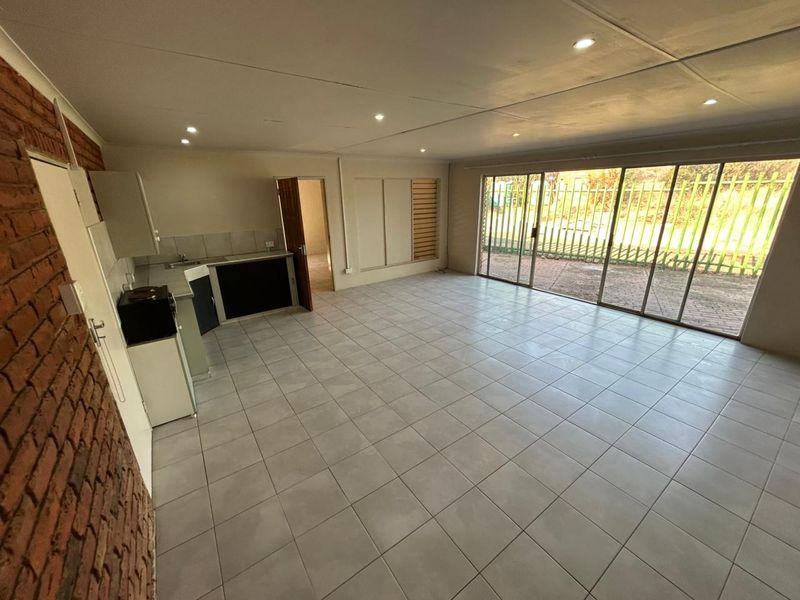 Spacious open-plan living area featuring tiled flooring, an exposed brick feature wall, integrated kitchen cabinetry, and large sliding glass doors leading to the exterior.