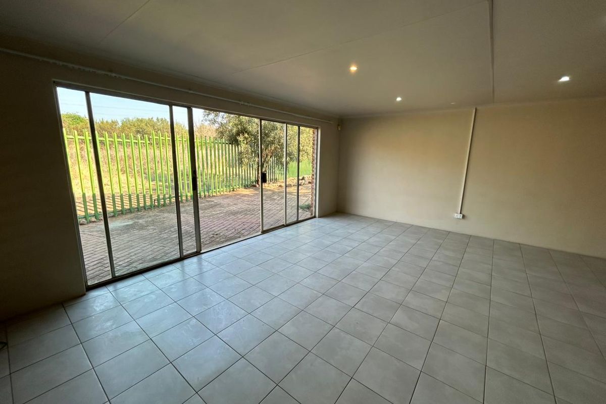 A spacious, empty living area featuring neutral tiled flooring, recessed lighting, and large sliding glass doors providing direct access to the outdoor patio area.