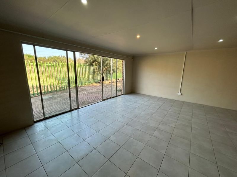 A spacious, empty living area featuring neutral tiled flooring, recessed lighting, and large sliding glass doors providing direct access to the outdoor patio area.