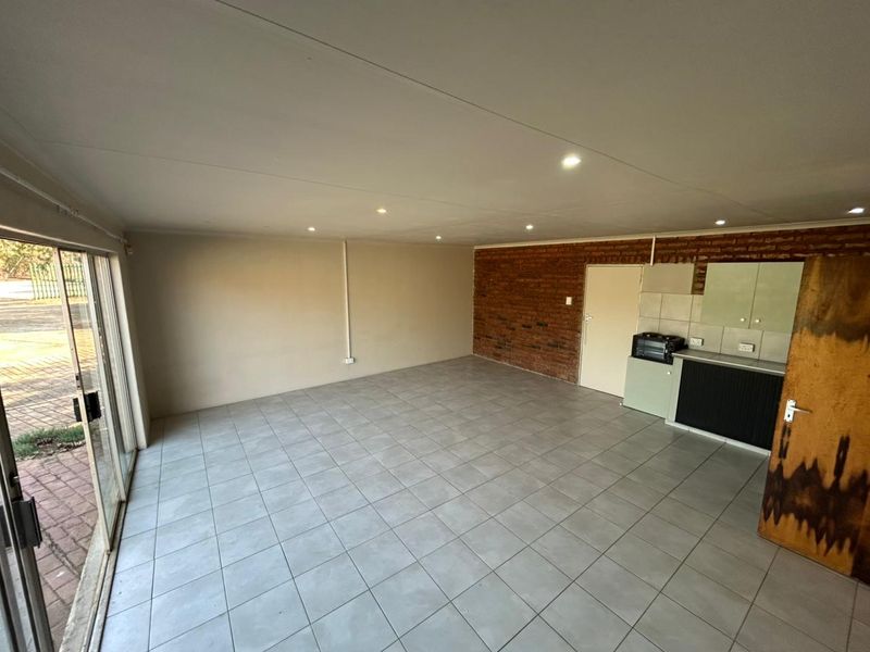 Open-plan living area featuring tiled floors, an exposed brick feature wall, recessed lighting, and direct access to the exterior via sliding glass doors.
