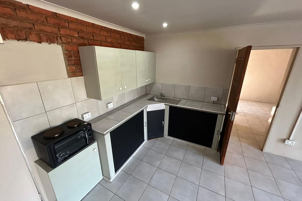 Compact kitchen featuring tiled flooring, built-in cabinetry, a stainless steel sink, and an exposed brick feature wall.