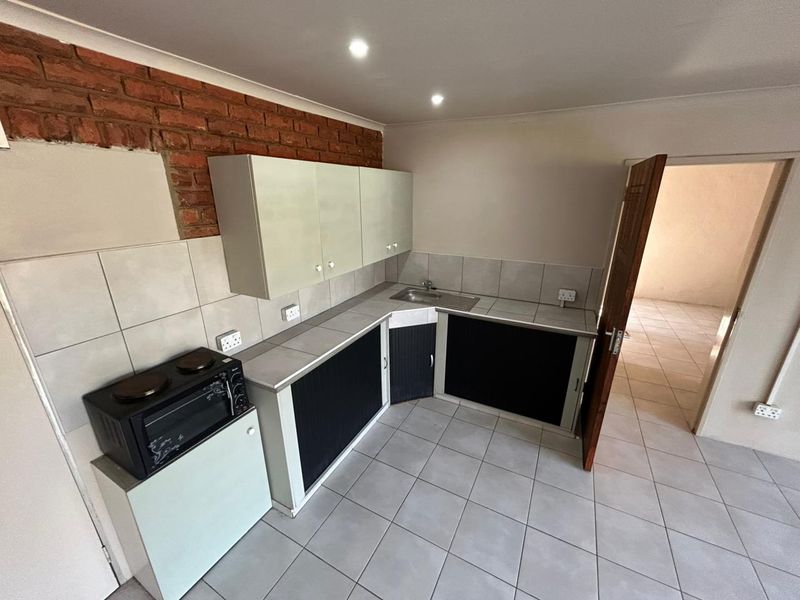 Compact kitchen featuring tiled flooring, built-in cabinetry, a stainless steel sink, and an exposed brick feature wall.