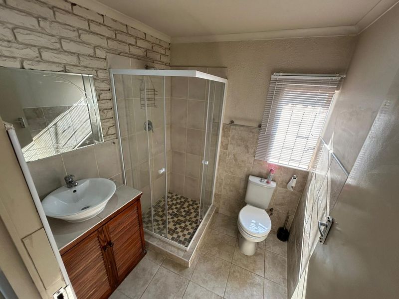 A functional bathroom featuring a shower enclosure, vanity cabinet with vessel sink, toilet, and a decorative brick feature wall with tiled finishes.
