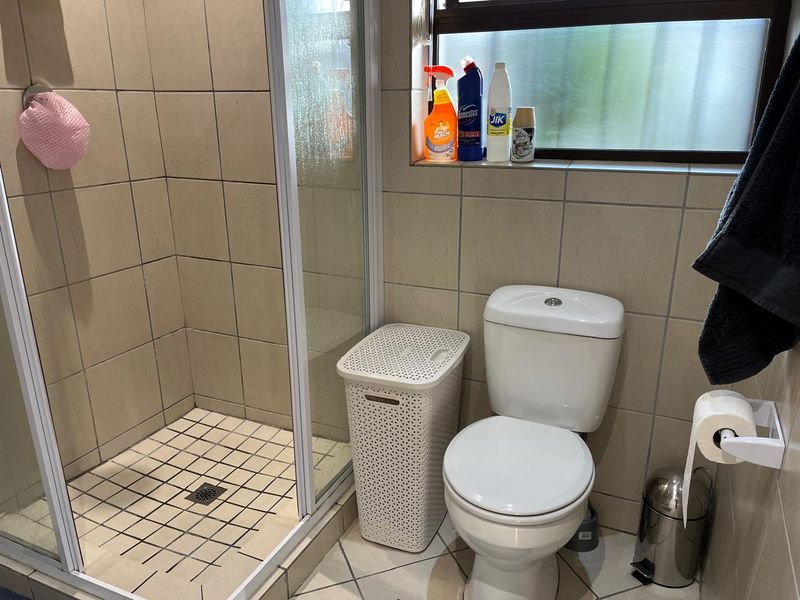 A functional bathroom featuring a tiled shower enclosure, a standard toilet, and tiled flooring with a window for natural light.
