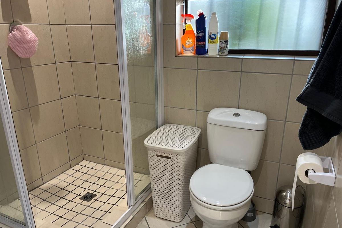 A functional bathroom featuring a tiled shower enclosure, a standard toilet, and tiled flooring with a window for natural light.