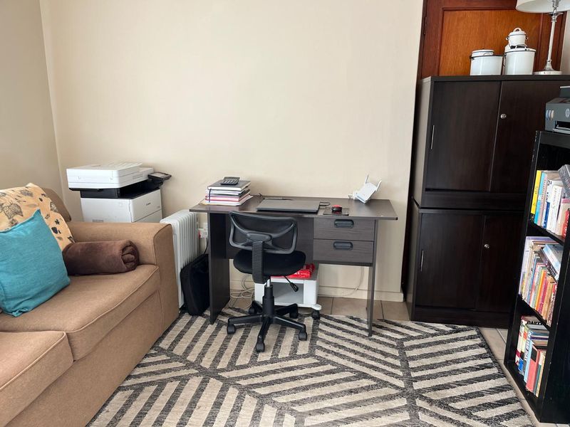 A functional living area featuring neutral wall tones and tiled flooring, currently utilized as a multi-purpose workspace.