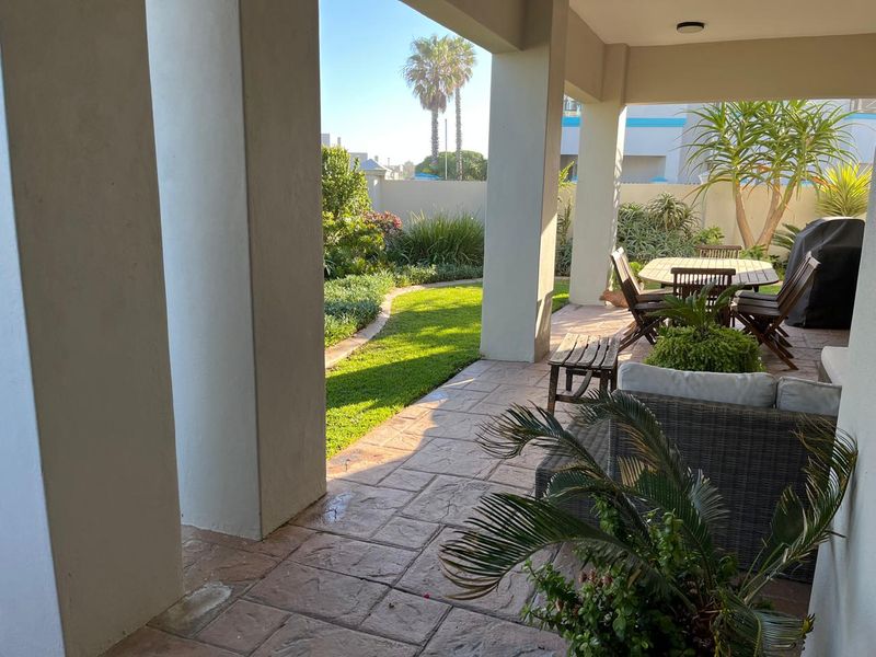 A covered patio area featuring stamped concrete flooring and structural pillars, overlooking a well-maintained private garden.