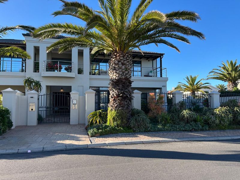 A well-maintained modern apartment building exterior featuring a paved driveway, secure wrought iron gate, and upper-level balconies with stainless steel railings.