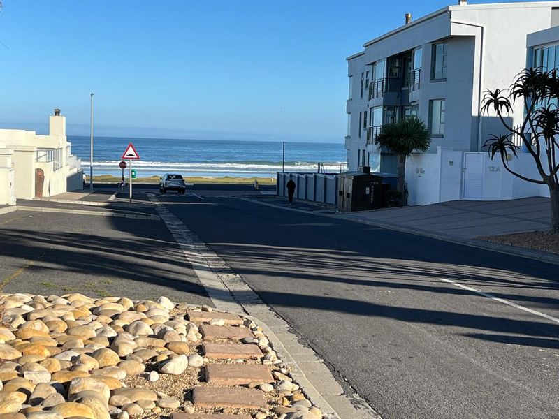 A street view showing the coastal apartment building exterior, paved driveway, and proximity to the ocean.