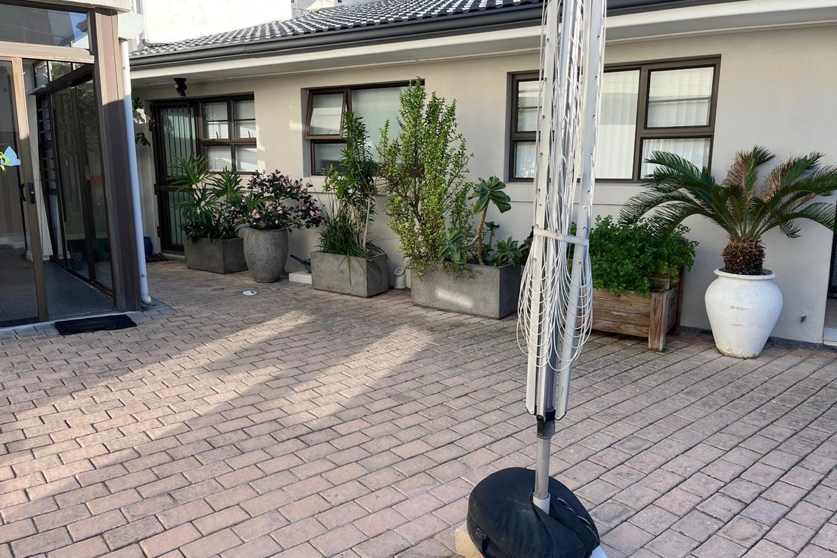 A paved rear patio area featuring a tiled roof, aluminium window frames, and a secure entrance, providing a functional outdoor space.