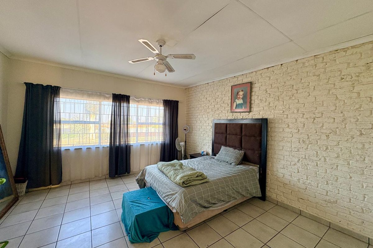 Spacious bedroom featuring tiled flooring, a ceiling fan, and a distinctive white-painted exposed brick feature wall with security bars on the windows.