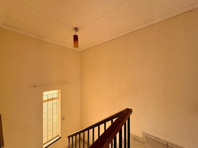 A staircase landing area featuring a wooden handrail, tiled flooring, and a window with security bars, showing signs of wear on the walls.