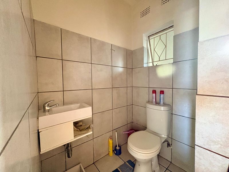 A compact guest bathroom featuring tiled walls, a wall-mounted basin, and a standard toilet with a small window for ventilation.