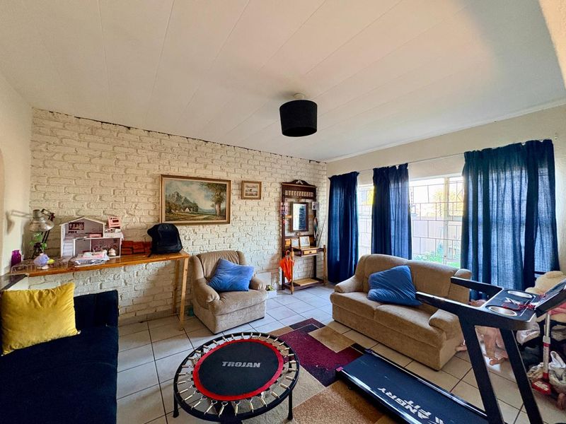 A living room featuring an exposed white-painted brick wall, tiled flooring, and large windows allowing natural light into the space.