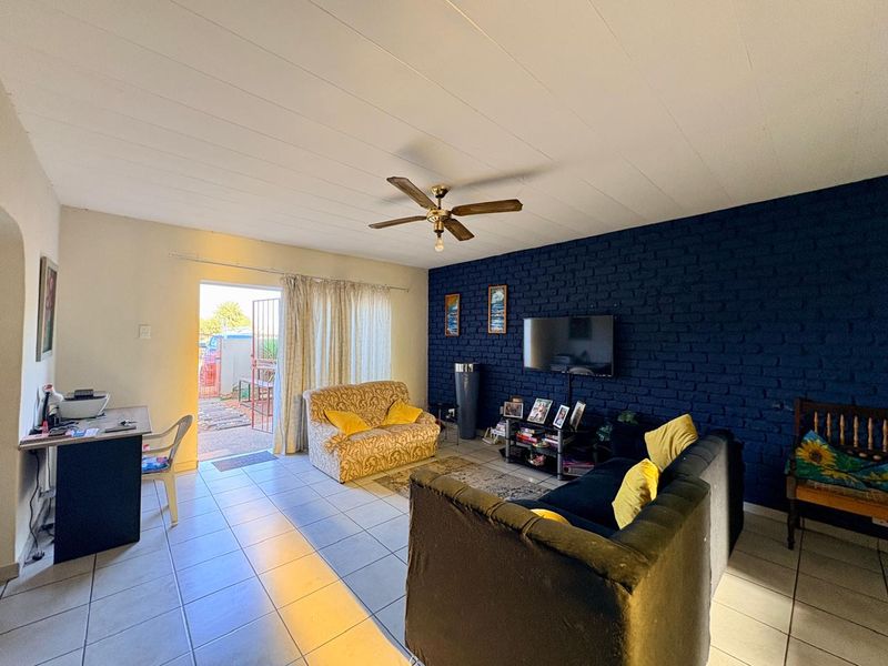 A living room featuring tiled flooring, a ceiling fan, and a dark blue exposed brick feature wall with direct access to an outdoor area.