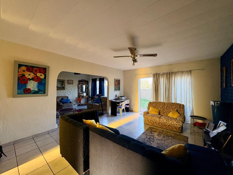 Spacious living area featuring tiled flooring, a ceiling fan, and an arched transition to an adjacent room with exposed brickwork and garden access.