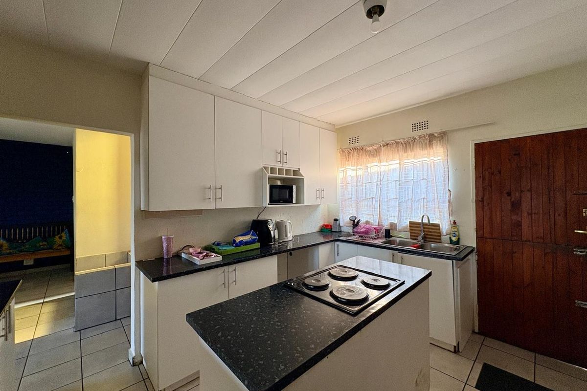 Functional kitchen featuring white cabinetry, dark laminate countertops, an integrated electric hob, and tiled flooring with direct access to adjacent living space.