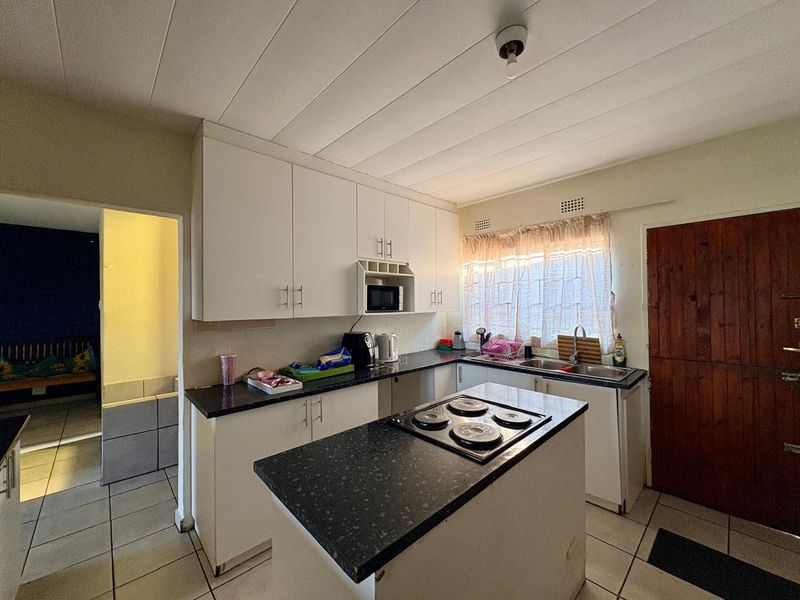 Functional kitchen featuring white cabinetry, dark laminate countertops, an integrated electric hob, and tiled flooring with direct access to adjacent living space.