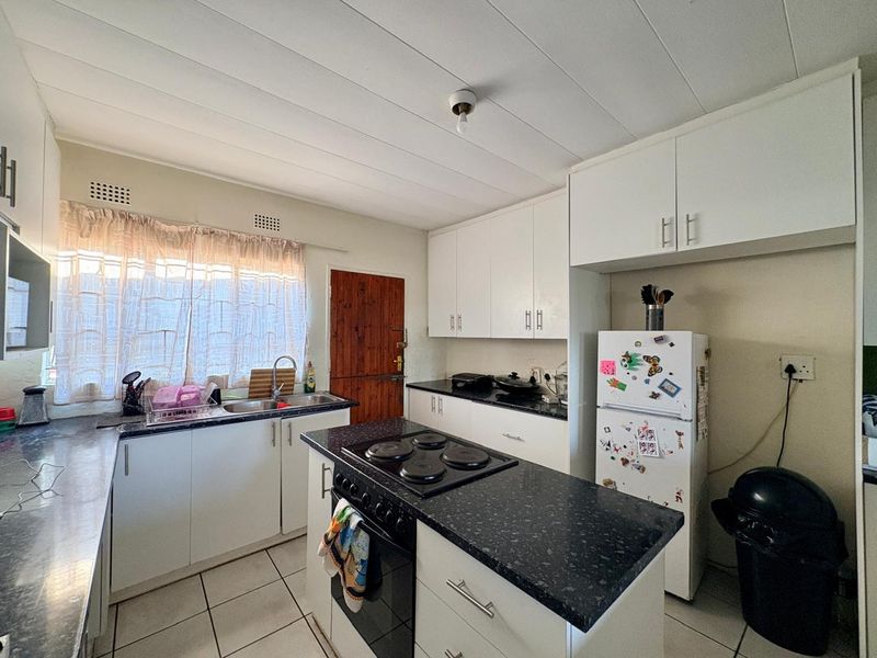 Functional kitchen featuring white cabinetry, dark laminate countertops, a central island with an electric hob, and tiled flooring.