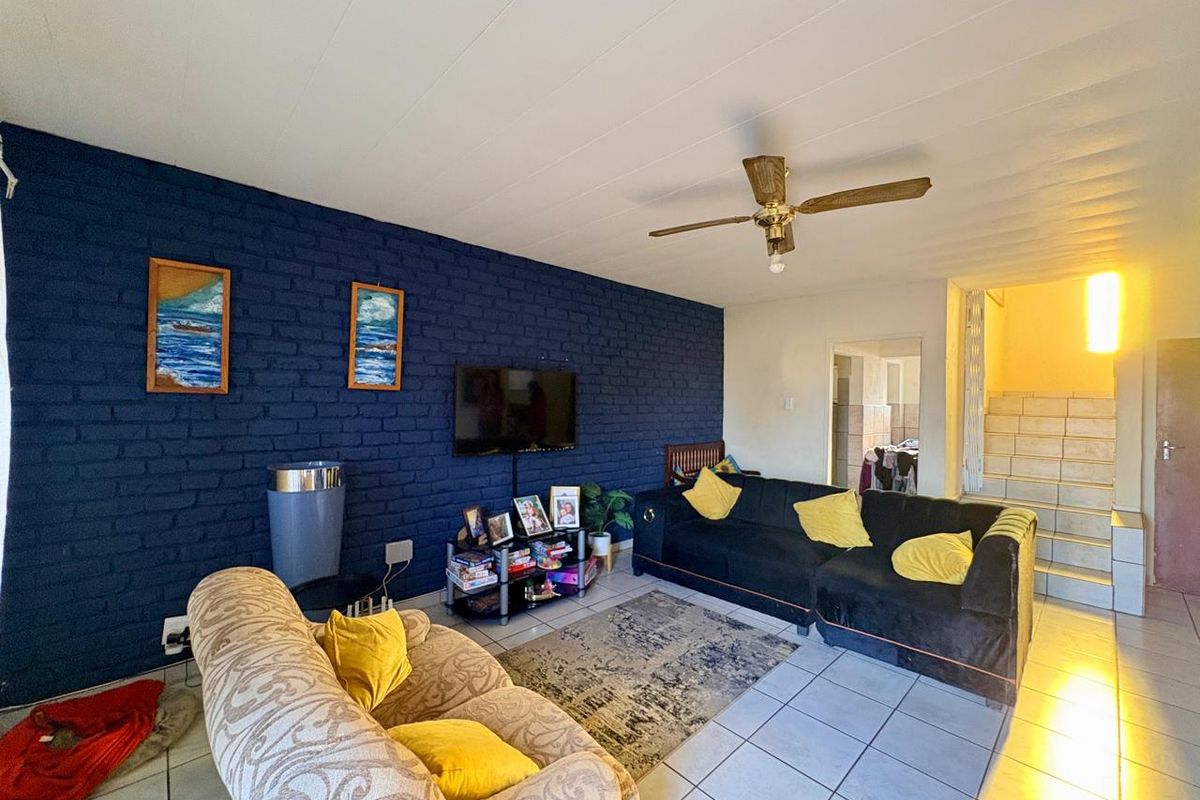 A living room featuring a dark blue exposed brick feature wall, tiled flooring, and a ceiling fan, with an adjacent staircase leading to another level.