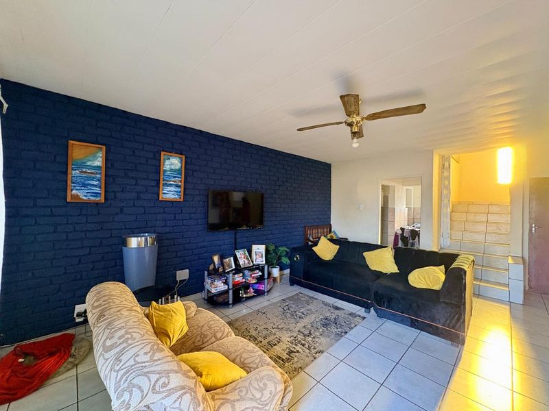 A living room featuring a dark blue exposed brick feature wall, tiled flooring, and a ceiling fan, with an adjacent staircase leading to another level.