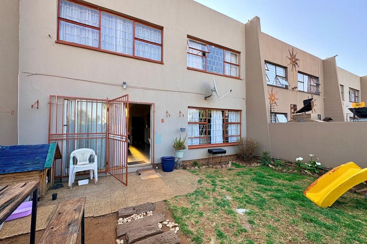 Rear exterior view of the townhouse featuring a paved patio area, small garden space, and security-fitted windows.