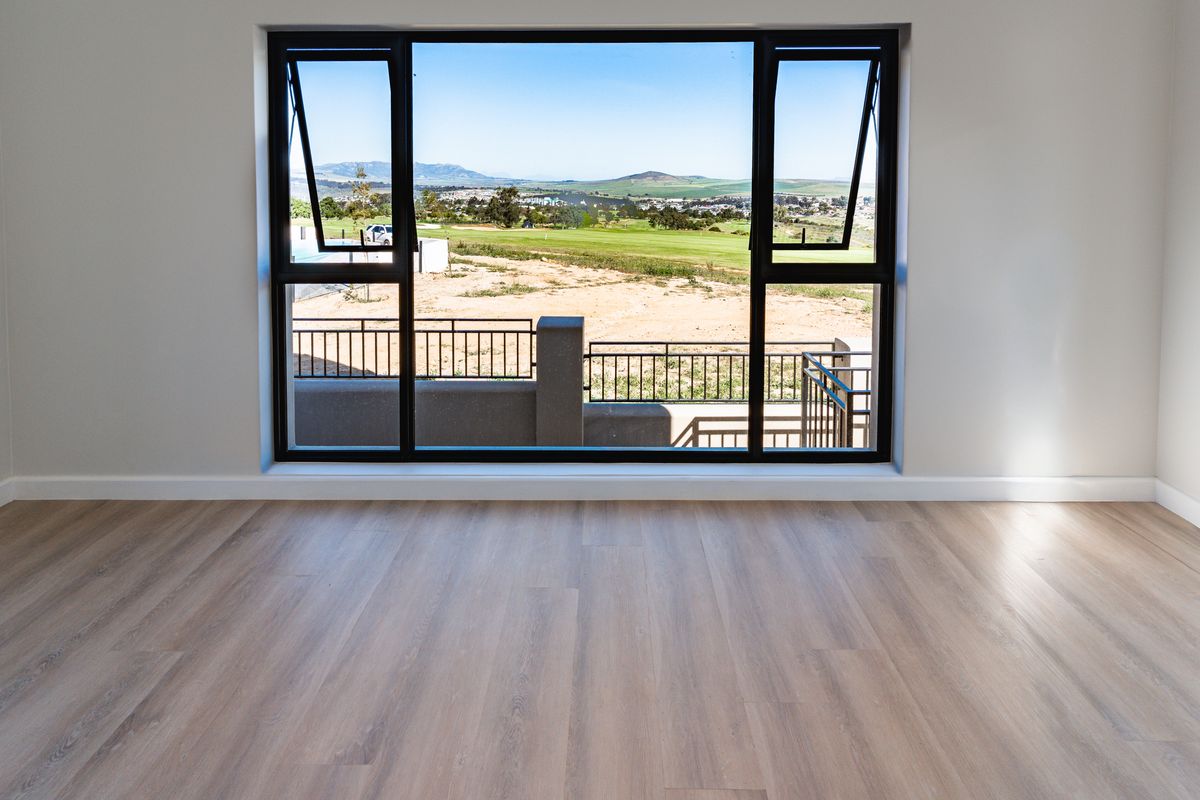 A bright, empty bedroom featuring modern laminate flooring and a large window offering expansive views of the surrounding landscape.