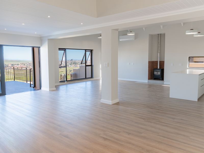 Spacious open-plan living area featuring wood-look flooring, a modern fireplace, kitchen island, and seamless access to a balcony with scenic views.