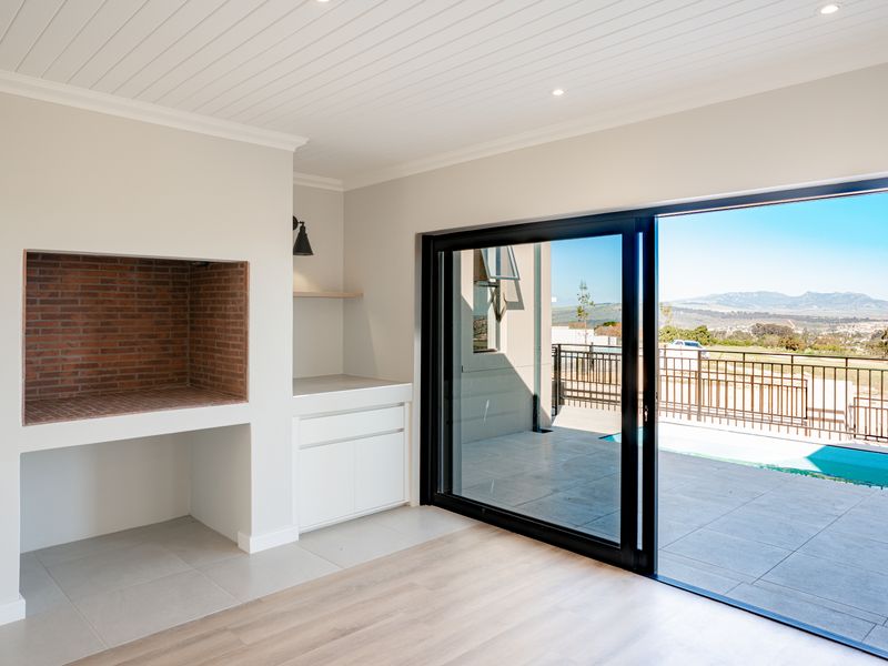 Bright living area featuring a built-in brick braai, modern cabinetry, and large sliding doors opening to a patio with pool and scenic views.