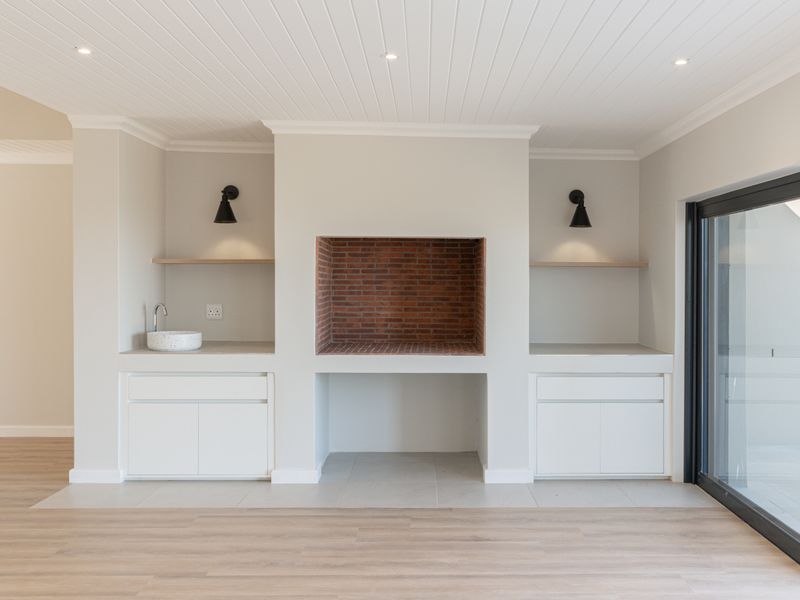 A bright living area featuring a built-in brick braai, custom cabinetry with integrated sink, and modern sliding glass doors leading to the outdoors.