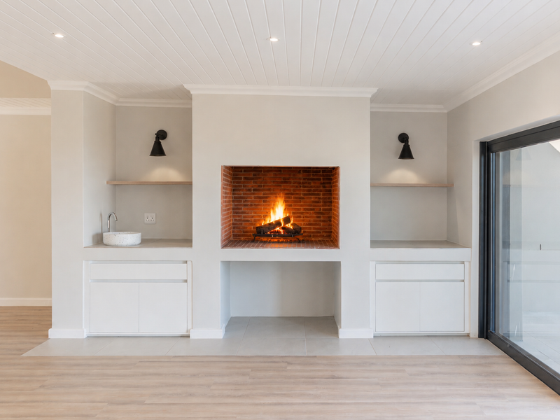 A bright living area featuring a central brick fireplace, built-in cabinetry with an integrated sink, floating shelves, and large sliding doors leading outdoors.