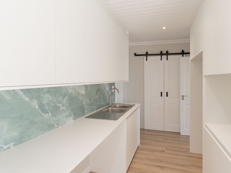 A clean, modern scullery featuring white built-in cabinetry, a stainless steel double sink, a decorative splashback, and a sliding barn door.