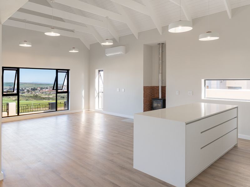 Spacious open-plan living area featuring a vaulted ceiling with exposed beams, a modern kitchen island, wood-burning fireplace, and expansive views.