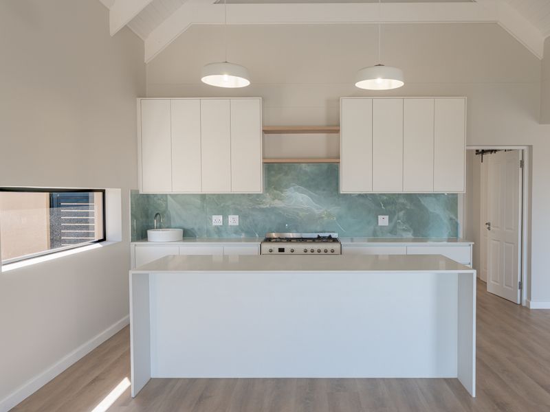 Modern kitchen featuring a central island, sleek white cabinetry, stone splashback, gas cooktop, and vaulted ceilings with pendant lighting.
