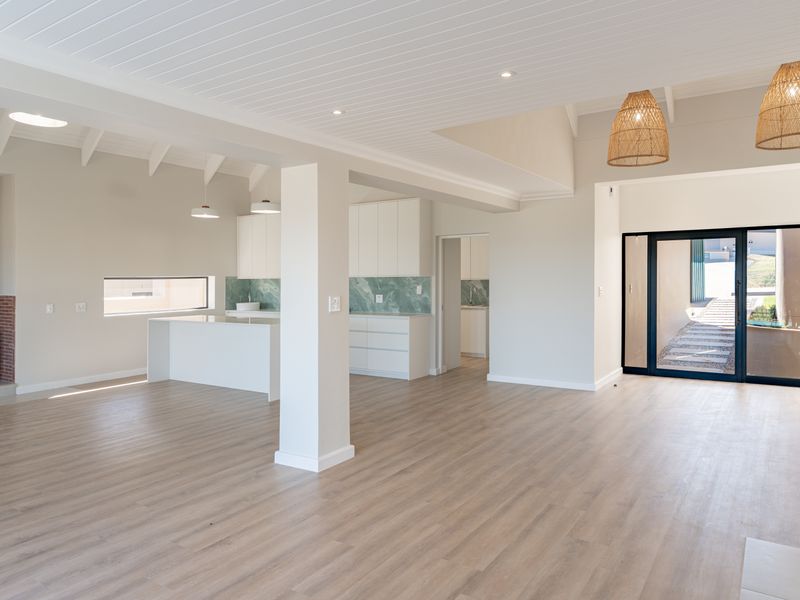 Spacious open-plan living area featuring a modern kitchen with stone backsplash, wood-burning fireplace, and seamless access to the outdoor patio.